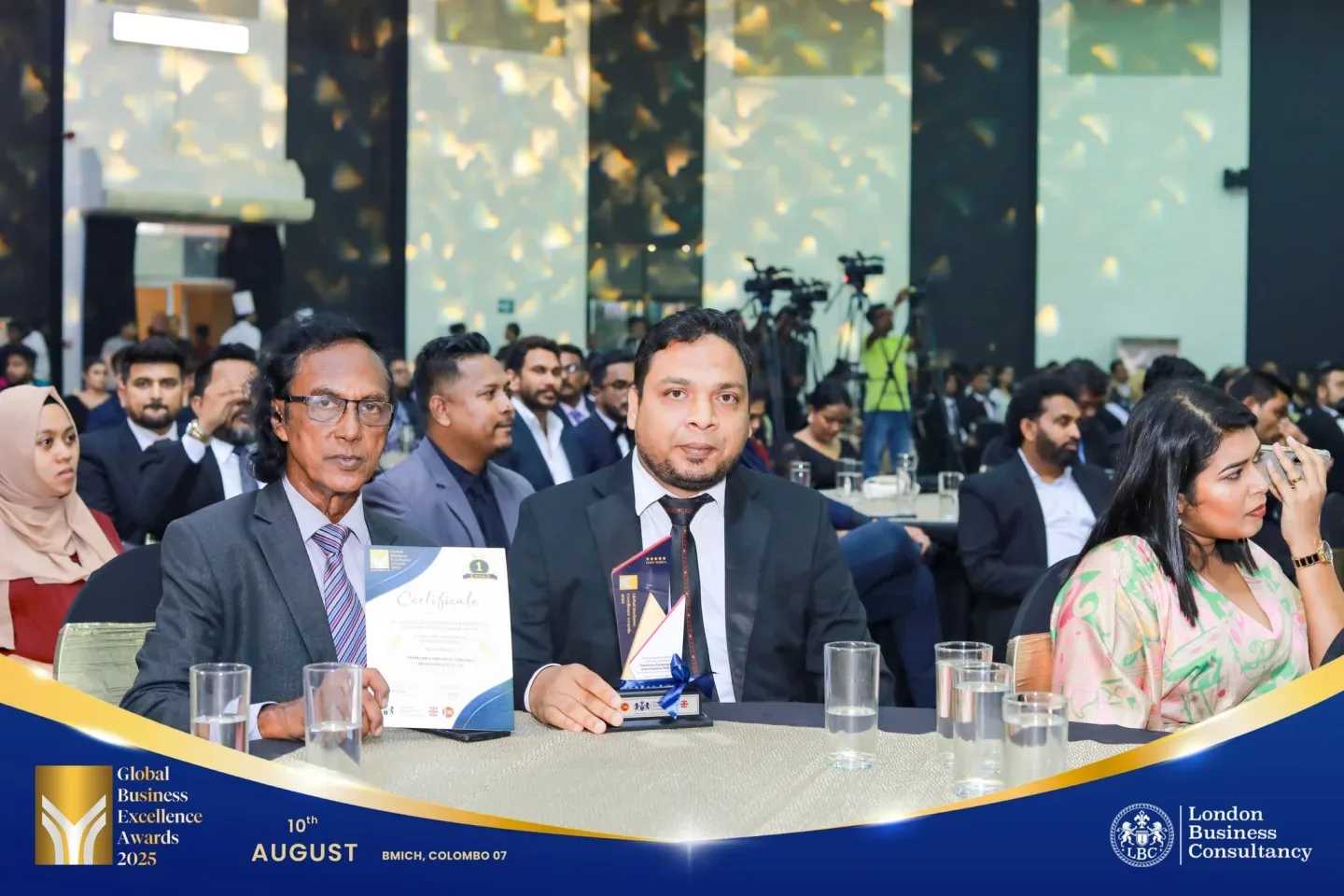 Global Business Excellence Awards recipient seated with a trophy and certificate