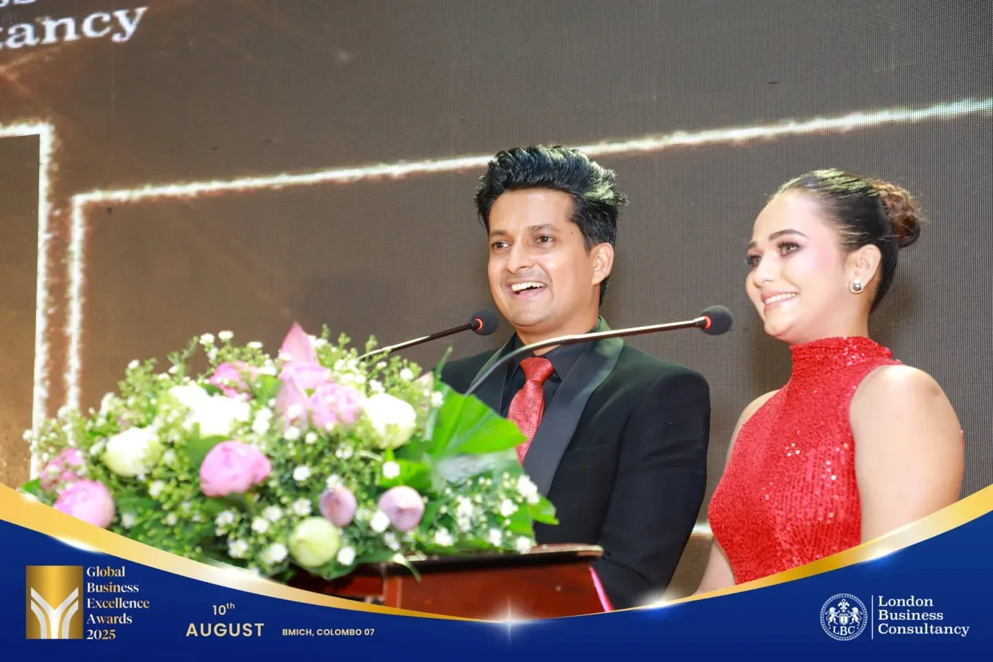 Two hosts speaking from the Global Business Excellence Awards stage